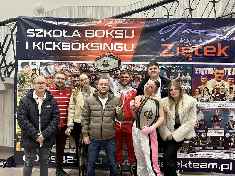Janek Matyjaszczyk z pasem mistrza Polski wśród zawodników i trenerów Team Ziętek, pod banerem szkoły boksu i kickboxingu